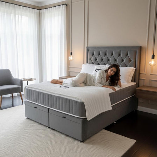 Woman lying on a gray upholstered bed in a modern bedroom.